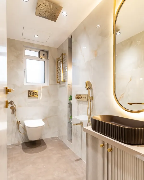 Luxury in every little detail. This contemporary bathroom blends serene white and beige-toned tiles with opulent gold fittings, creating a space that feels both refreshing and indulgent. The sleek SS mirror frame adds a crisp modern edge.