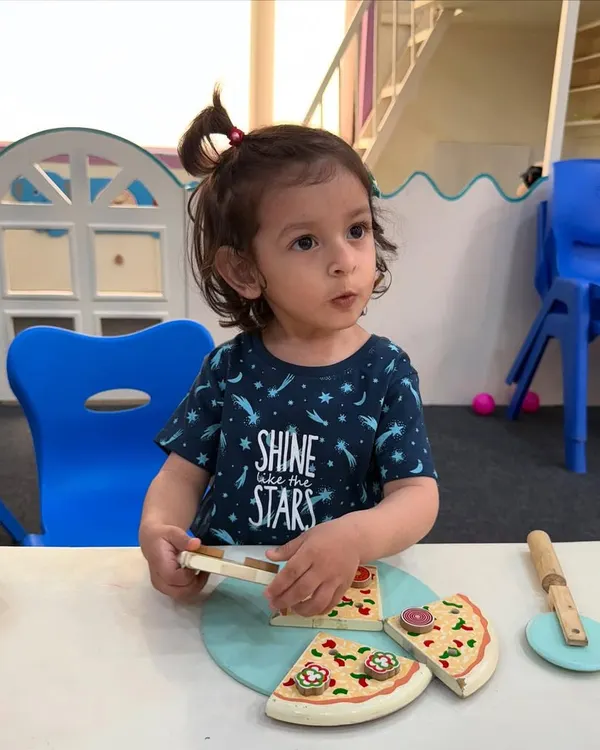 Our little stars learn best when they are involved. Here, a child is engaged in a pretend play activity with a wooden pizza set, which helps in developing social and fine motor skills.