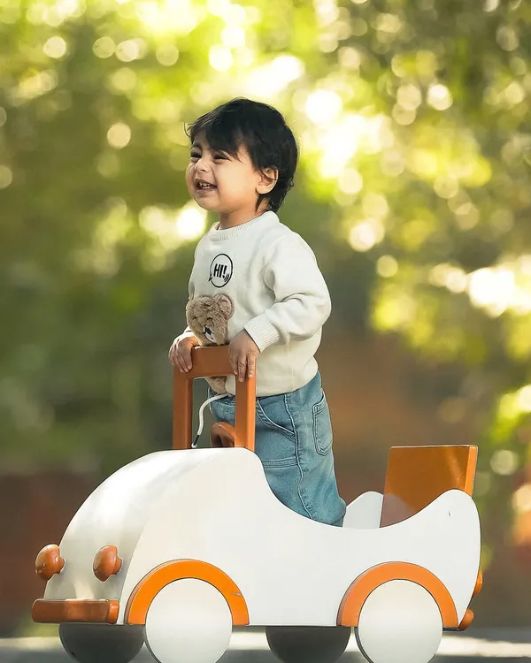 A little boy's face lights up with a huge smile as he plays in his toy car during an outdoor session. The beautiful, soft background and natural light make his joyful expression the star of the photo.