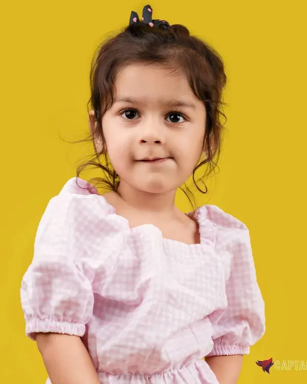 A charming close-up portrait of a young girl against a vibrant yellow background. The soft lighting and her direct, sweet expression make this a perfect shot for a kid's portfolio or family album.