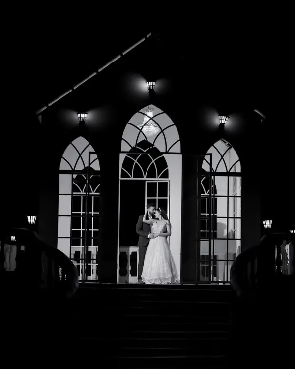 A dramatic and timeless black and white shot of the couple at the entrance of a grand building. The strong silhouettes and architectural lines create a powerful, cinematic image.
