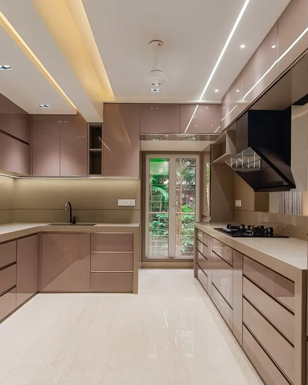 A beautiful and spacious U-shaped kitchen with rose-gold toned, back-painted glass panels. The layout provides ample counter space and storage, with integrated lighting to create a luxurious and functional cooking environment.