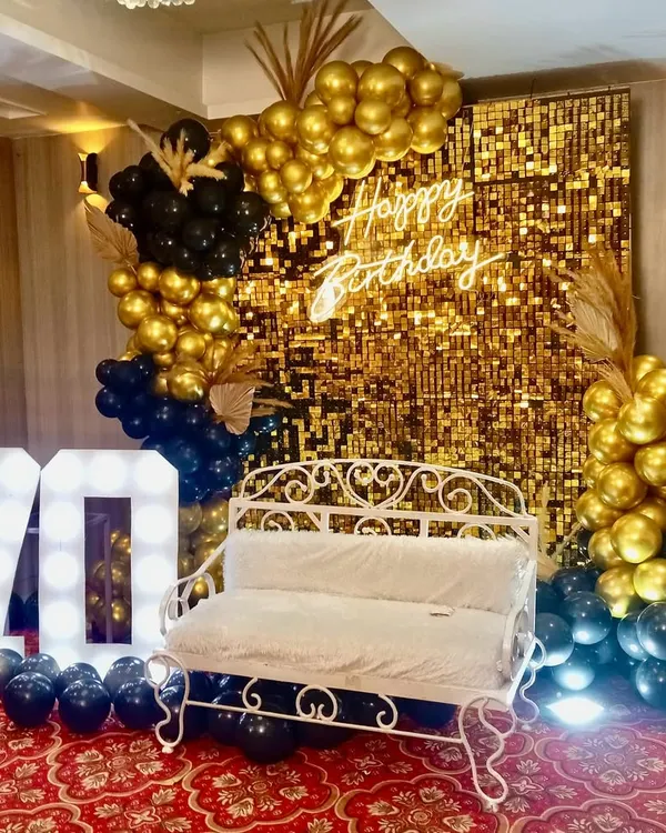 For a glamorous 70th birthday, we designed this stunning photo booth with a gold shimmer wall, a custom 'Happy Birthday' neon sign, and bold marquee numbers. The black and gold balloon arrangement adds a touch of sophisticated fun.
