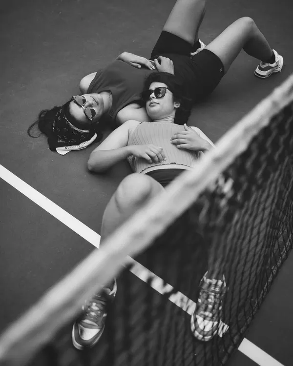 An unconventional portrait of two people on a tennis court. The high angle and the lines of the court create a strong graphic composition, focusing on a moment of shared stillness.