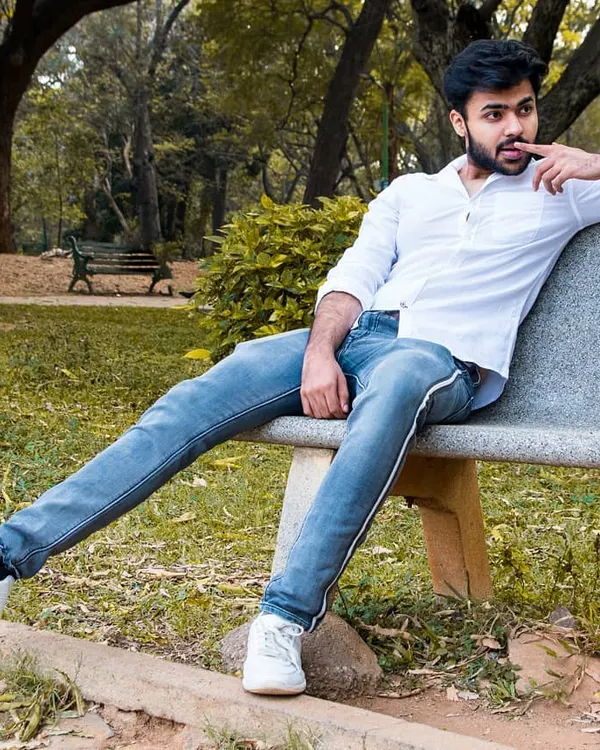 A relaxed outdoor portrait of a man sitting on a park bench. The natural setting and his casual pose create a candid and approachable feel for this men's portfolio shot.
