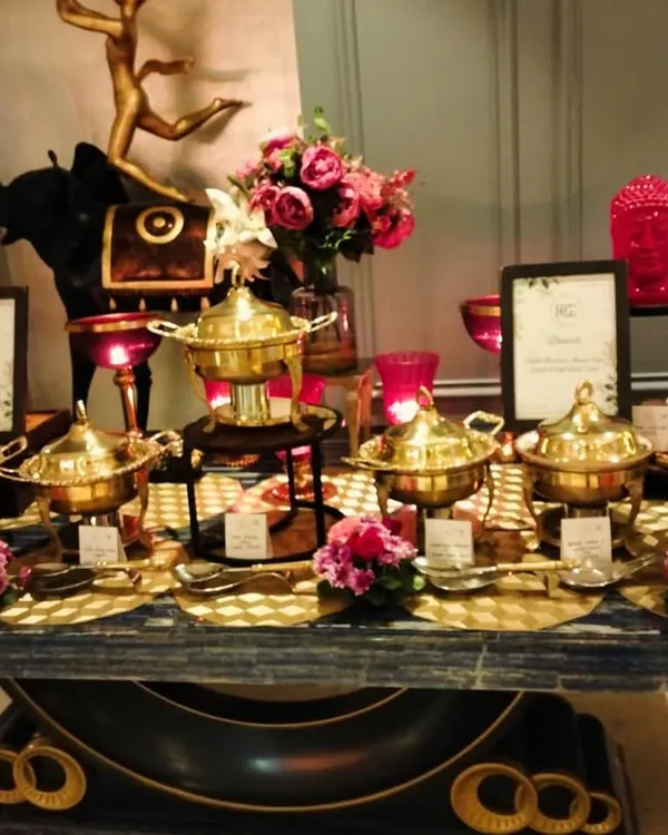 An opulent Indian food buffet featuring our signature brass serving dishes. The setup is enhanced with elegant floral arrangements and decorative pieces, creating a truly luxurious feel for a house party.