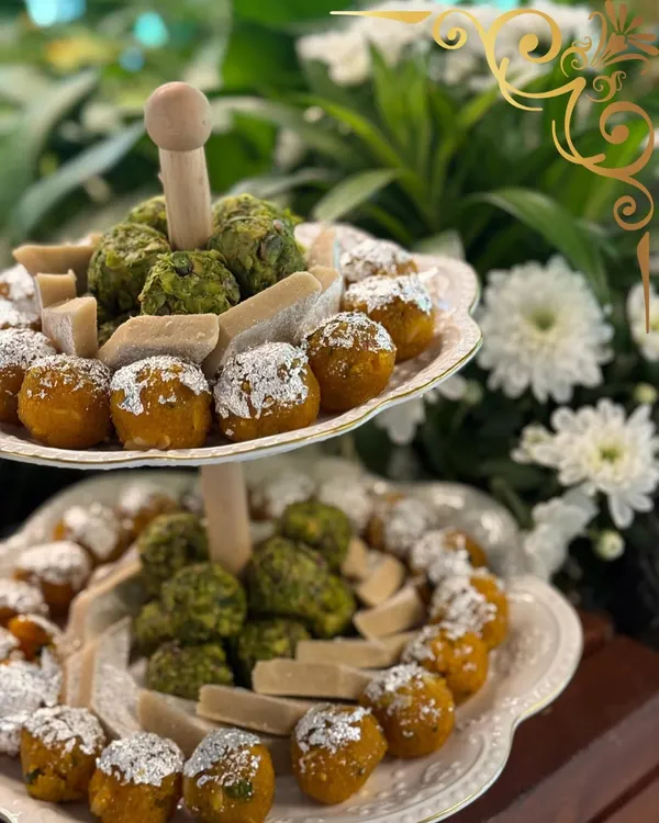 A tiered stand of traditional Indian sweets, or mithai, featuring pistachio barfi and motichoor ladoo, elegantly dusted with silver varq.