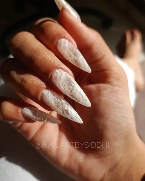 A set of dramatic, extra-long stiletto nails with an encapsulated white marble and foil design, showing the beautiful shape and length that can be achieved.