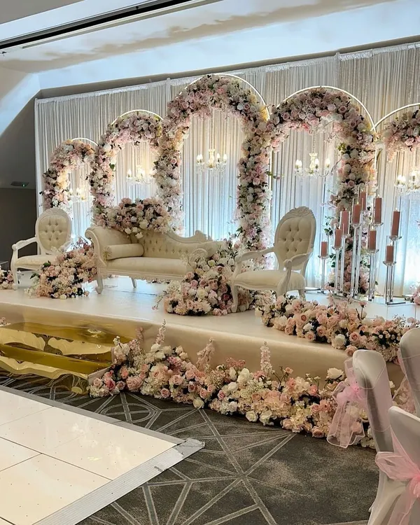 A breathtaking fairytale stage for a wedding reception, featuring cascading pink and white floral arches, elegant seating, and soft, romantic lighting to create a truly magical atmosphere.