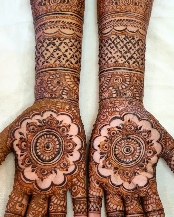 A gorgeous and intricate design for the bride's sister. The central mandala on the palm is a classic choice, surrounded by detailed patterns that extend up the forearm.