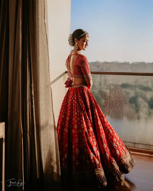 A bride in her magnificent red lehenga, taking a quiet moment on the balcony to look out at the view. This silhouette against the morning light creates a breathtaking and pensive portrait.