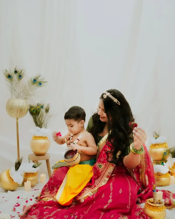 A beautiful 'Maiya aur Kanha' moment from a Janmashtami themed shoot. The mother and son are surrounded by peacock feathers and pots, creating a rich, festive scene.