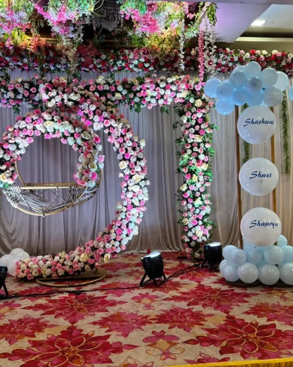 This grand floral stage was designed for a naming ceremony in a banquet hall. We created a large, crescent-shaped floral structure to frame the baby's cradle, using a mix of pink and white artificial roses for a lush, elegant look.