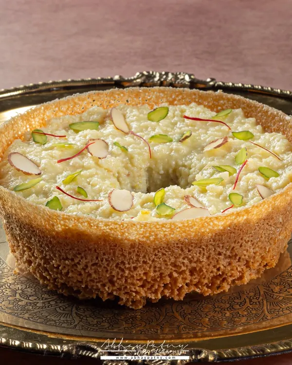 Ghewar is a festive delicacy, and I wanted to capture its royal feel. I used a traditional silver platter and soft lighting to highlight the intricate, porous texture and the delicate almond and saffron garnish.