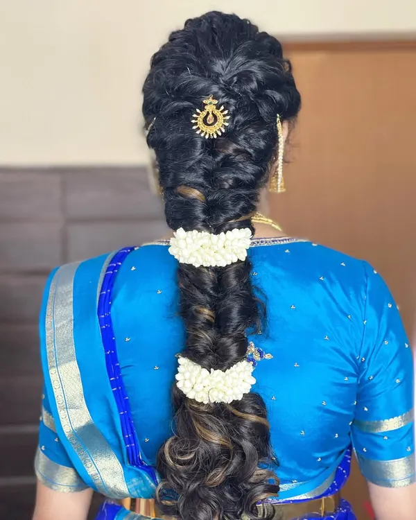 A detailed view of a beautiful, thick fishtail braid, accented with jasmine flowers and a traditional sun-shaped hair accessory. This hairstyle is perfect for a classic South Indian look.