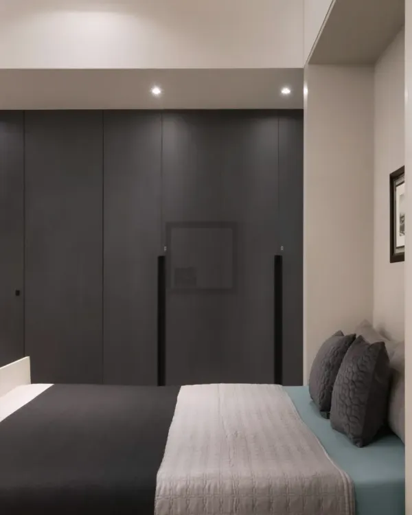 Here is an example of a floor-to-ceiling wardrobe in a dark grey finish that creates a calm, minimalist bedroom. The design features handleless doors for a clean look and a recessed niche for a television, perfectly integrating storage and media.