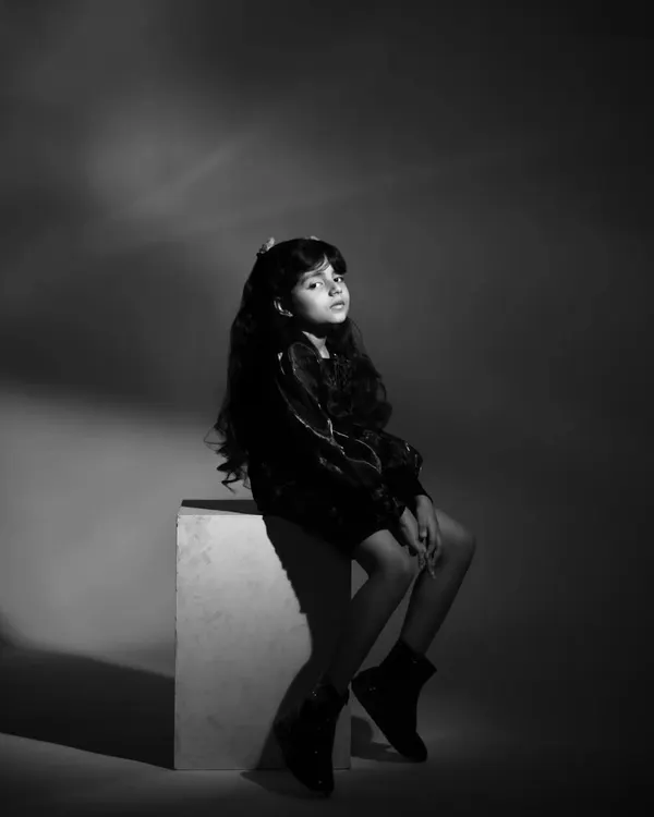 A dramatic black and white shot for a child's portfolio. The lighting and pose create a high-fashion feel, showcasing her ability to convey a serious and focused mood on camera.