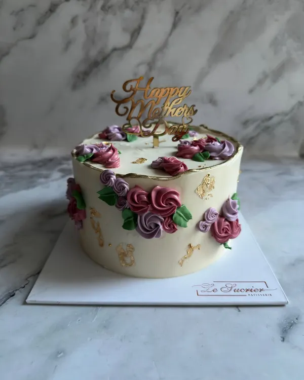This elegant Mother's Day cake is decorated with delicate, hand-piped buttercream flowers in shades of pink and purple, finished with a touch of edible gold leaf for a luxurious feel.