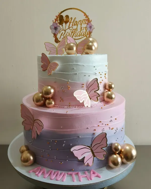This is one of my favorite designs, a beautiful two-tier butterfly cake. The ombre effect with different shades of purple and pink buttercream gives it a dreamy feel, and the delicate butterflies and gold spheres add a touch of magic. It's perfect for a first birthday or any elegant celebration.
