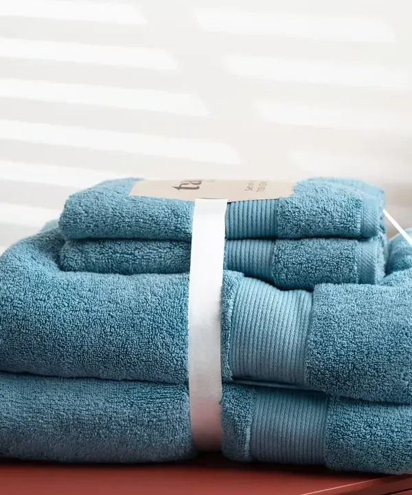 A neatly folded set of blue towels on a modern bathroom counter. We use clean lines and bright lighting to create fresh and appealing images for home essentials.