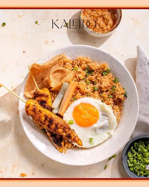 My authentic Nasi Goreng, a fragrant Indonesian fried rice. It's a complete meal served with chicken skewers, a dipping sauce, pickled salad, and crispy crackers for texture.