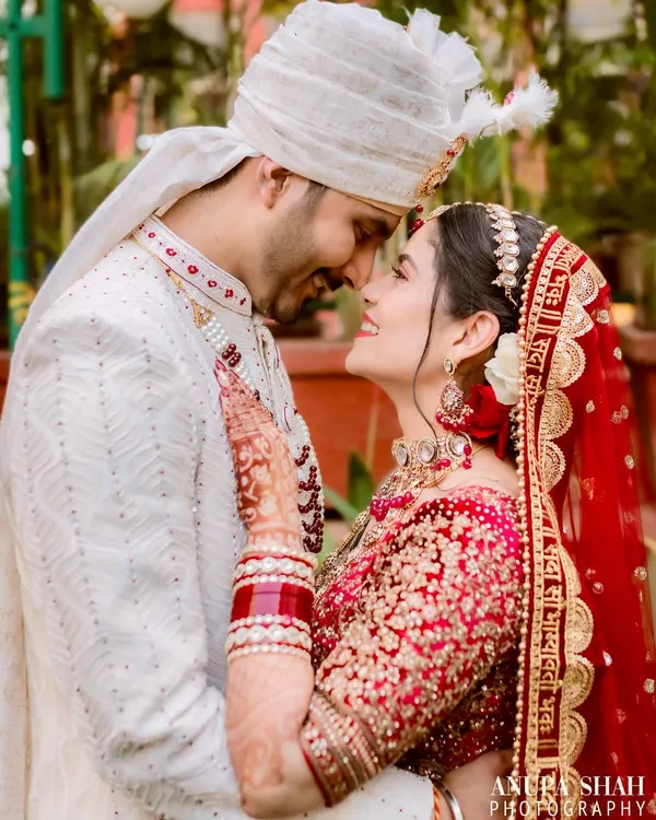 An intimate moment between the bride and groom, their foreheads touching in a gesture of pure affection. The soft lighting highlights their joyful expressions and the intricate details of their wedding attire.