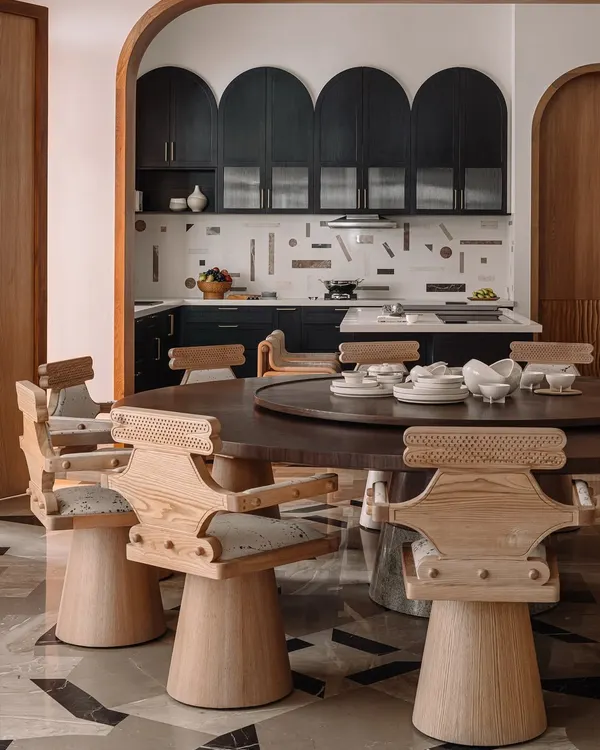 The dining room at Rehethaan, featuring impressive 'Kingpin' swivel chairs around a large circular table. The space opens up to the kitchen through a large, wood-framed archway.