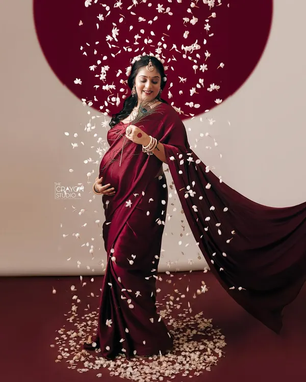 The flow of a beautiful red saree and a shower of petals create a sense of movement and celebration. This full length portrait captures the grace and power of the mother to be.