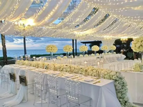 This all-white dining setup by the sea is the definition of elegance and is perfect for an exclusive corporate retreat or VIP dinner. The flowing drapery, fairy lights, and transparent chairs create a clean, sophisticated, and unforgettable ambiance.