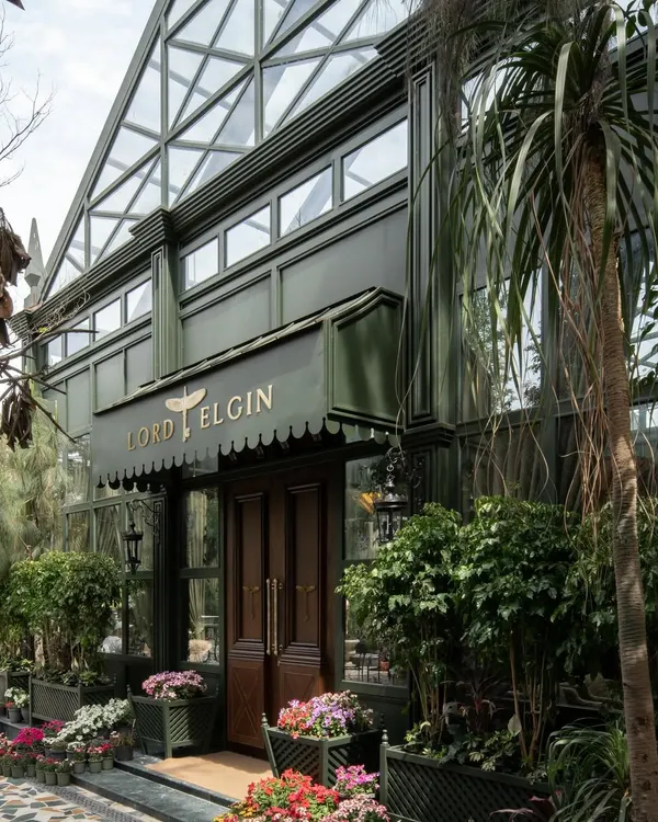 The exterior of the Lord Elgin Glasshouse, a striking green structure surrounded by vibrant flowers. The design immediately establishes the brand's identity as a lush, garden-like escape.