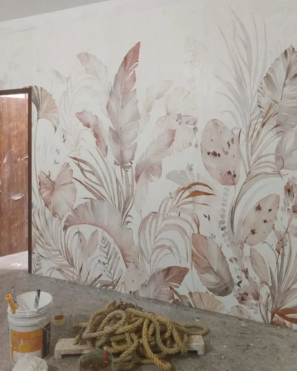 This botanical wallpaper features large, overlapping leaves in soft, muted tones. It’s a perfect example of an in-progress installation, showing how a nature-inspired mural can bring a sense of calm and elegance to a room.