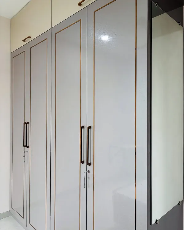 A sleek, modern wardrobe in a grey high-gloss finish with elegant gold inlay. This design includes a full-length mirror integrated into the side of the unit to save wall space.
