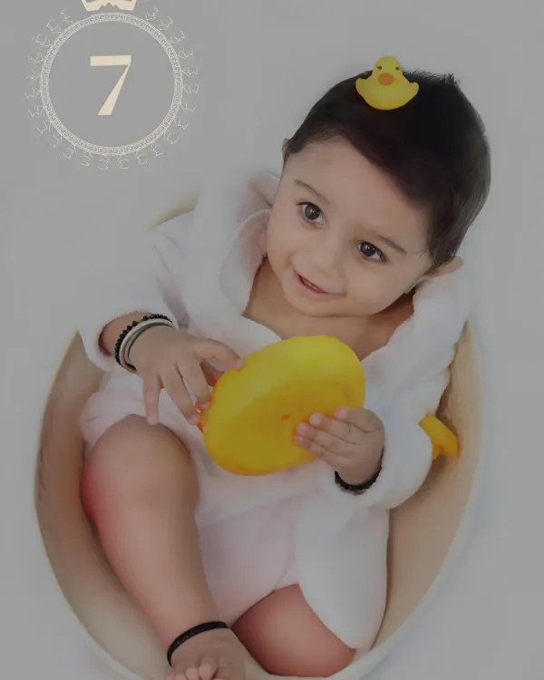 A happy baby in a little white bathrobe enjoys bath time play, holding a bright yellow rubber duck.