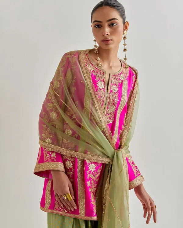 A stunning fuchsia pink kurta set featuring intricate gold embroidery on the sleeves and body, paired with wide-leg pants. The sheer green dupatta adds a beautiful contrast.