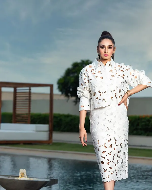 A high-fashion editorial photograph taken for a magazine cover. The composition places the model as a strong, central figure against the clean lines of the poolside location, emphasizing the unique laser-cut design of the white two-piece outfit.