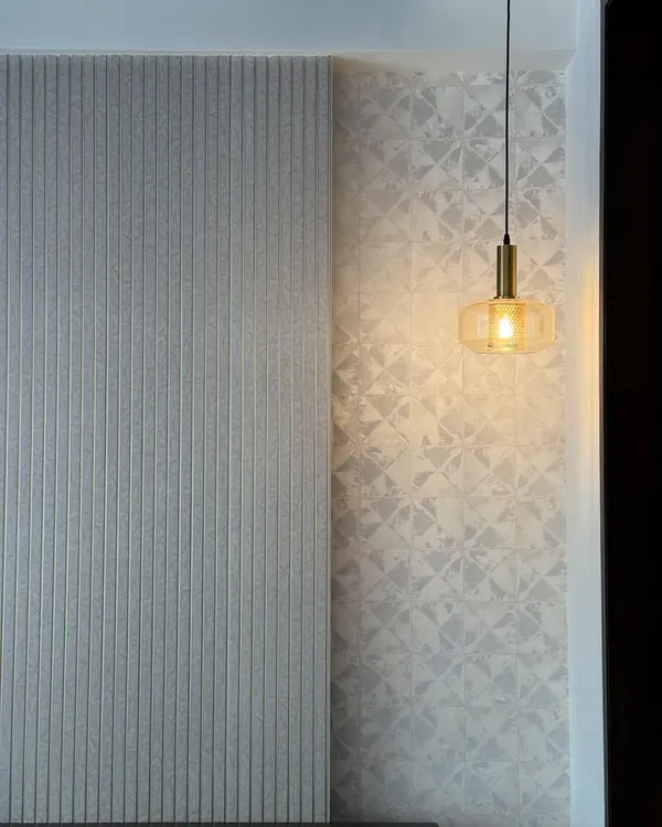 This wall’s got more lines than your ex during arguments. A close-up of a textured wall with vertical fluting next to a patterned wallpaper, lit by a single pendant.