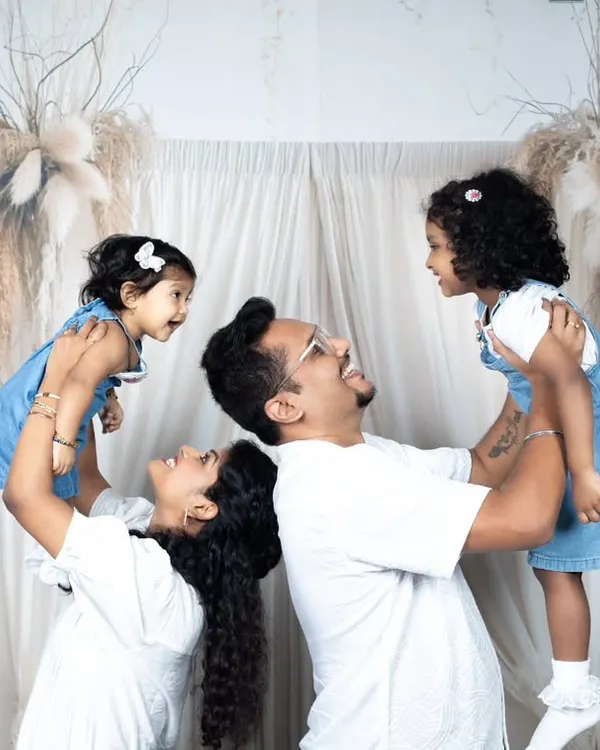 A fun and energetic family photo with parents lifting their two young daughters in the air, all smiling and laughing.