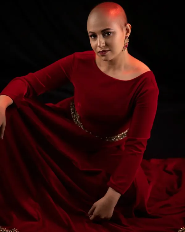 Bald, bold, and beautiful. This look is all about empowerment, featuring a strong, confident pose in a rich red velvet dress. The makeup is kept classic to let her powerful presence shine.