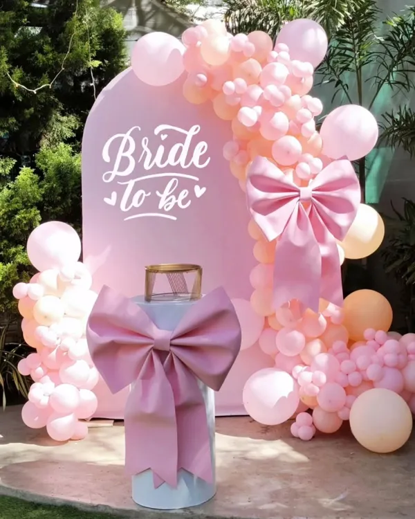 A closer look at a popular 'Bride to be' setup. The clean white arch provides a perfect canvas for the pretty pink balloon garland and statement bow, creating a beautiful focal point for photos.