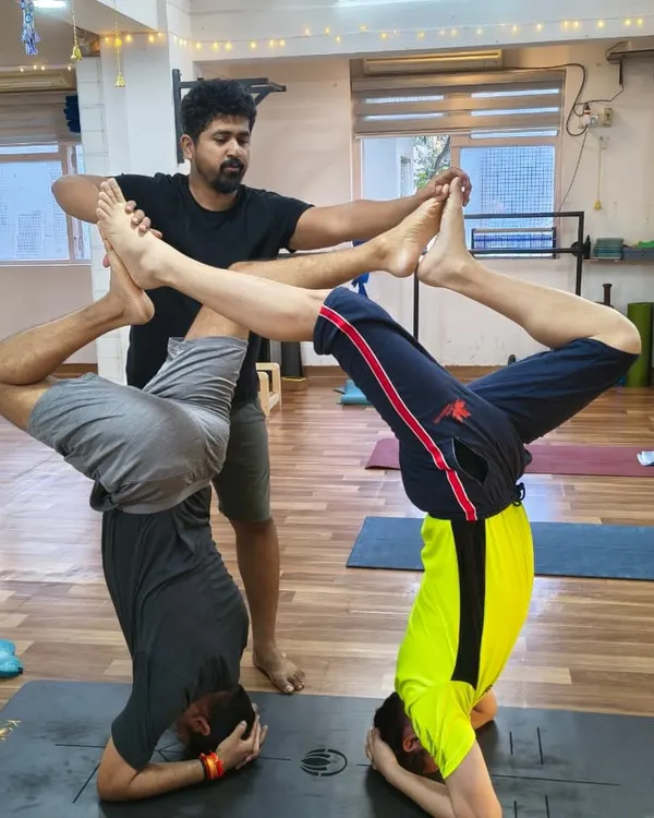 In our shala, we build strength and trust together. Here, I'm guiding two students through a synchronized headstand variation, focusing on precise alignment and mutual support. This is what our tribe is all about: lifting each other up.