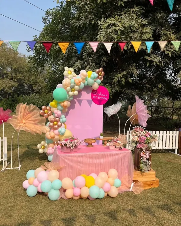 A beautiful pastel-themed birthday setup featuring a balloon arch and a dedicated cake table, ready for a special celebration.