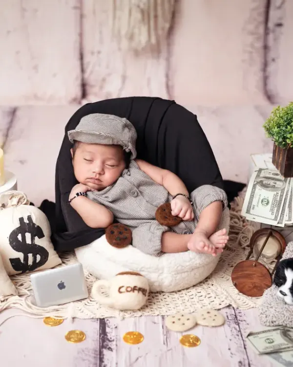 Meet the "Boss Baby"! This little one is styled in a grey outfit and cap, surrounded by props like money bags, a mini laptop, and a coffee mug.