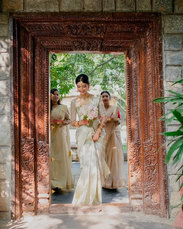 A radiant bride making her entrance at a day wedding, her soft ivory sari perfectly complementing the natural light and heritage venue.