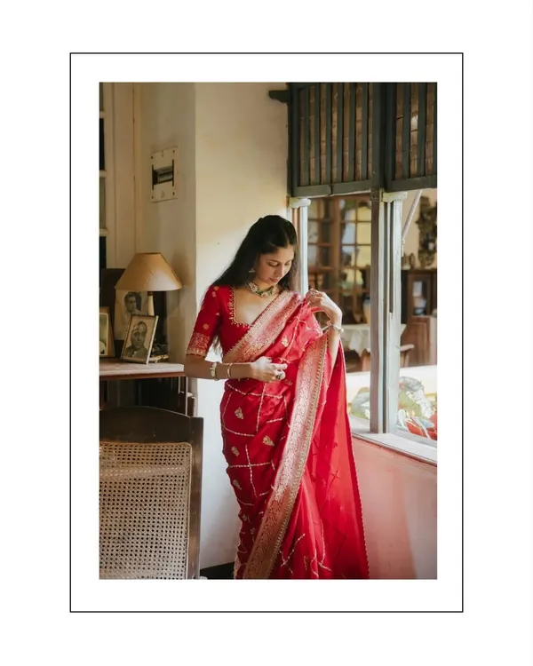A stunning portrait of the bride-to-be in a vibrant red saree, standing by a vintage window. The soft natural light and classic setting create a timeless and graceful image.