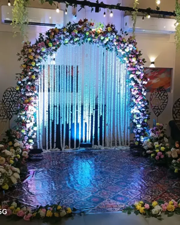A magnificent entrance arch for a wedding or reception. The arch is covered in colorful flowers and leads to a curtain of white jasmine strings, creating a magical entryway.