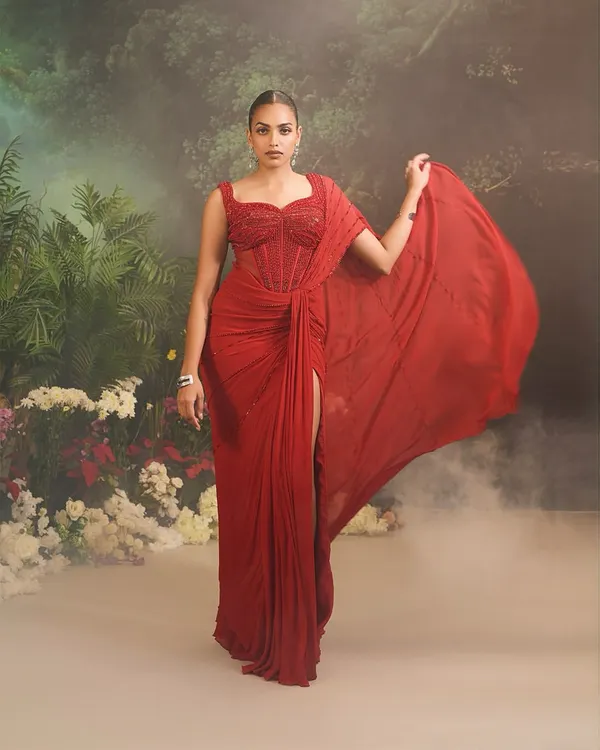 This is our Stardust Saree Set, the epitome of modern glamour. The ensemble features a striking, fully embellished corset blouse paired with a beautifully draped saree in a bold red, complete with a thigh-high slit for a contemporary edge.