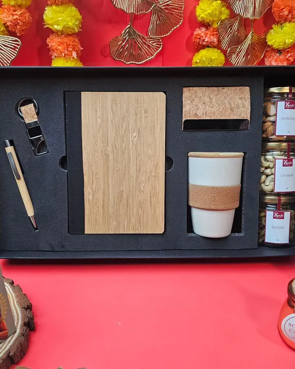 An elegant corporate Diwali gift set. This hamper includes a bamboo-finish diary and pen, a ceramic mug, and jars of premium dry fruits, all presented in a sleek black box.
