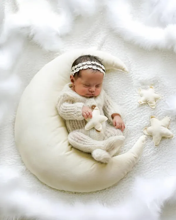 A sweet dream captured forever. This newborn girl, dressed in a cozy knit outfit and delicate headband, sleeps peacefully on our popular moon prop, creating a truly magical infant portrait.