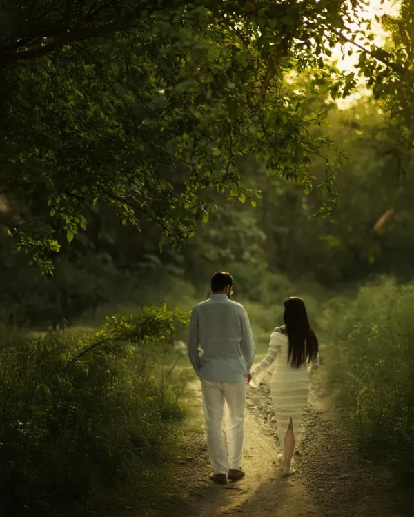 Walking together into a new chapter, hand in hand. This shot, taken on a rustic path surrounded by lush greenery, captures the journey of partnership with the golden sun filtering through the trees, symbolizing a bright future.