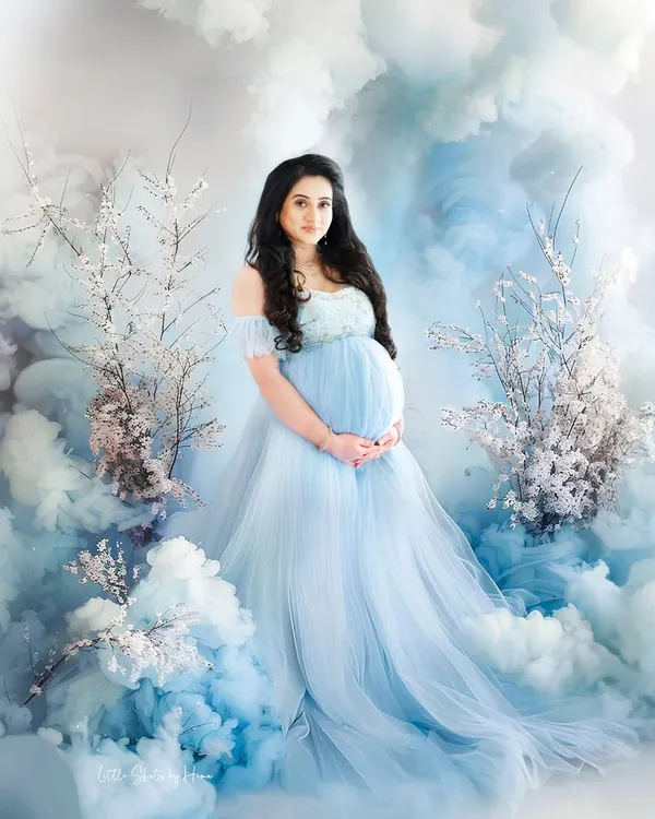 A magical maternity portrait where the mother-to-be is surrounded by a sea of blue clouds and cherry blossoms. She wears a matching light blue gown, creating a truly dreamy and ethereal scene.